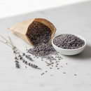Pure dried lavender buds in a white ceramic bowl on a marble surface with lavender sprigs