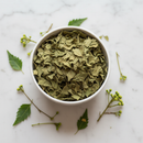 Dried neem leaves cut and sifted in a white ceramic bowl on marble surface with botanical accents