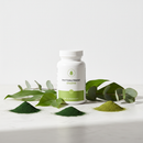 Genestra Phyto Greens Caps supplement bottle on white marble surface with spirulina and green botanical accents