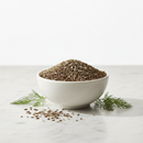 Whole Ajwain carom seeds in a white ceramic bowl on marble with herb sprigs and scattered seeds