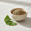 Ginkgo biloba leaves, cut and sifted, in a cream ceramic bowl on white marble surface with fresh ginkgo leaf accents