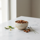 Raw whole almonds in a ceramic bowl on white marble surface