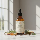 100mL amber glass bottle of Orange Sciatica Relief Massage Oil on white marble with botanical accents