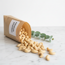 Whole raw cashews on a white marble surface with kraft paper bag