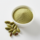 Cardamom seed powder in a white ceramic bowl with whole green cardamom pods on white background